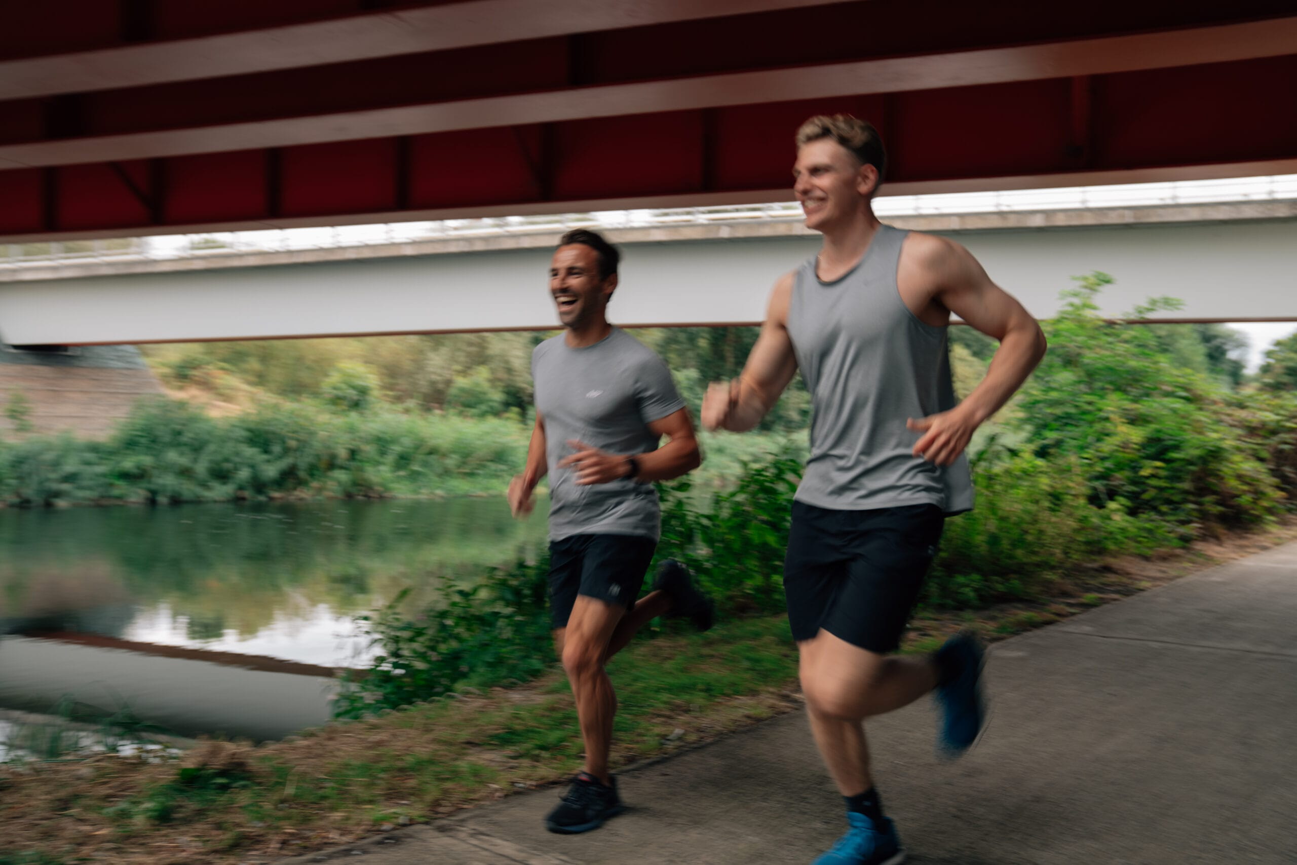 two men smiling running under a bridge