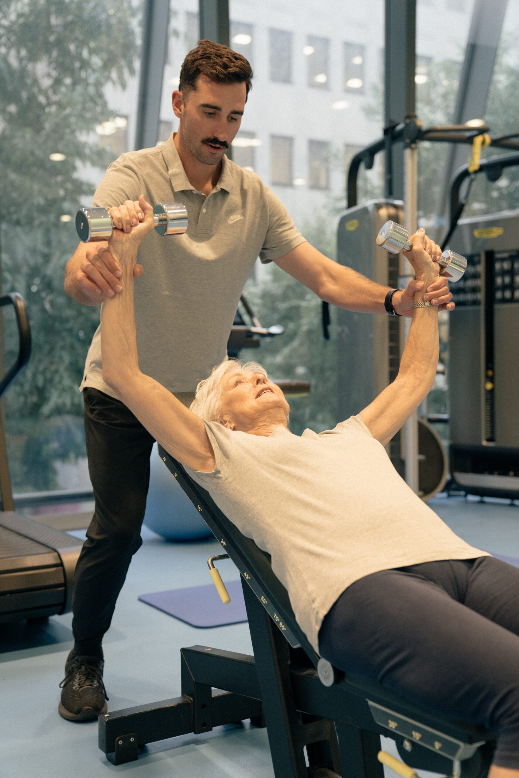clinician supporting older woman with weights