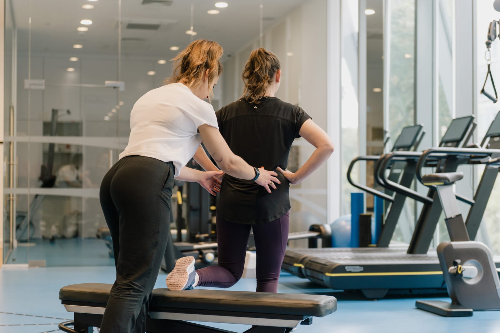 clinician holding patient's hips, one leg on bench in physio recovery gym