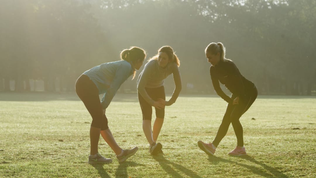 three women stretching their hamstrings in a field