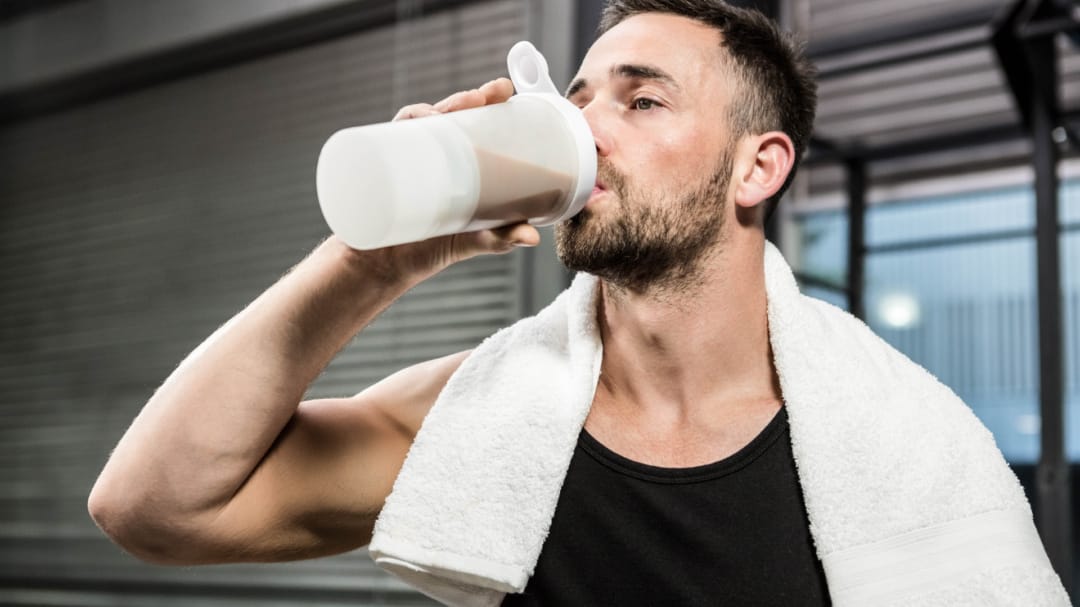 close up of man drinking a protein drink with a towel round his neck